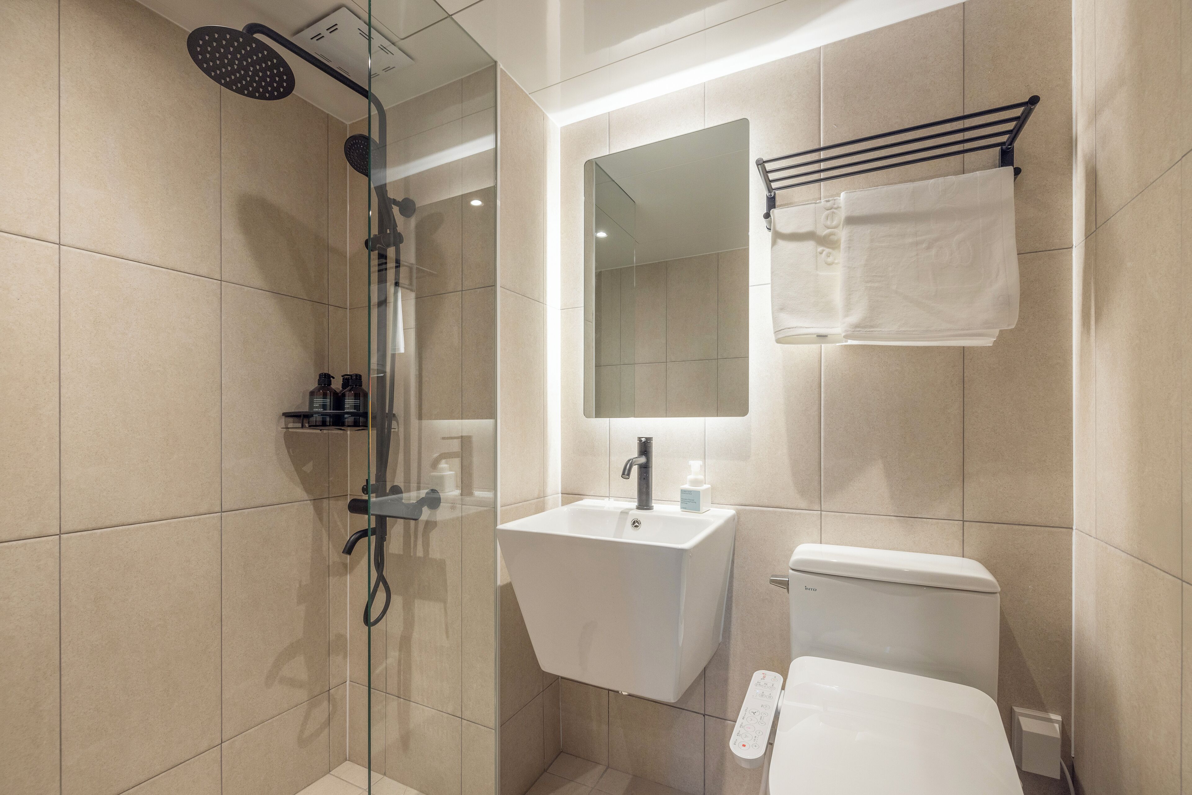 A modern bathroom with a glass-enclosed shower, a white sink, a mirror, and a toilet.