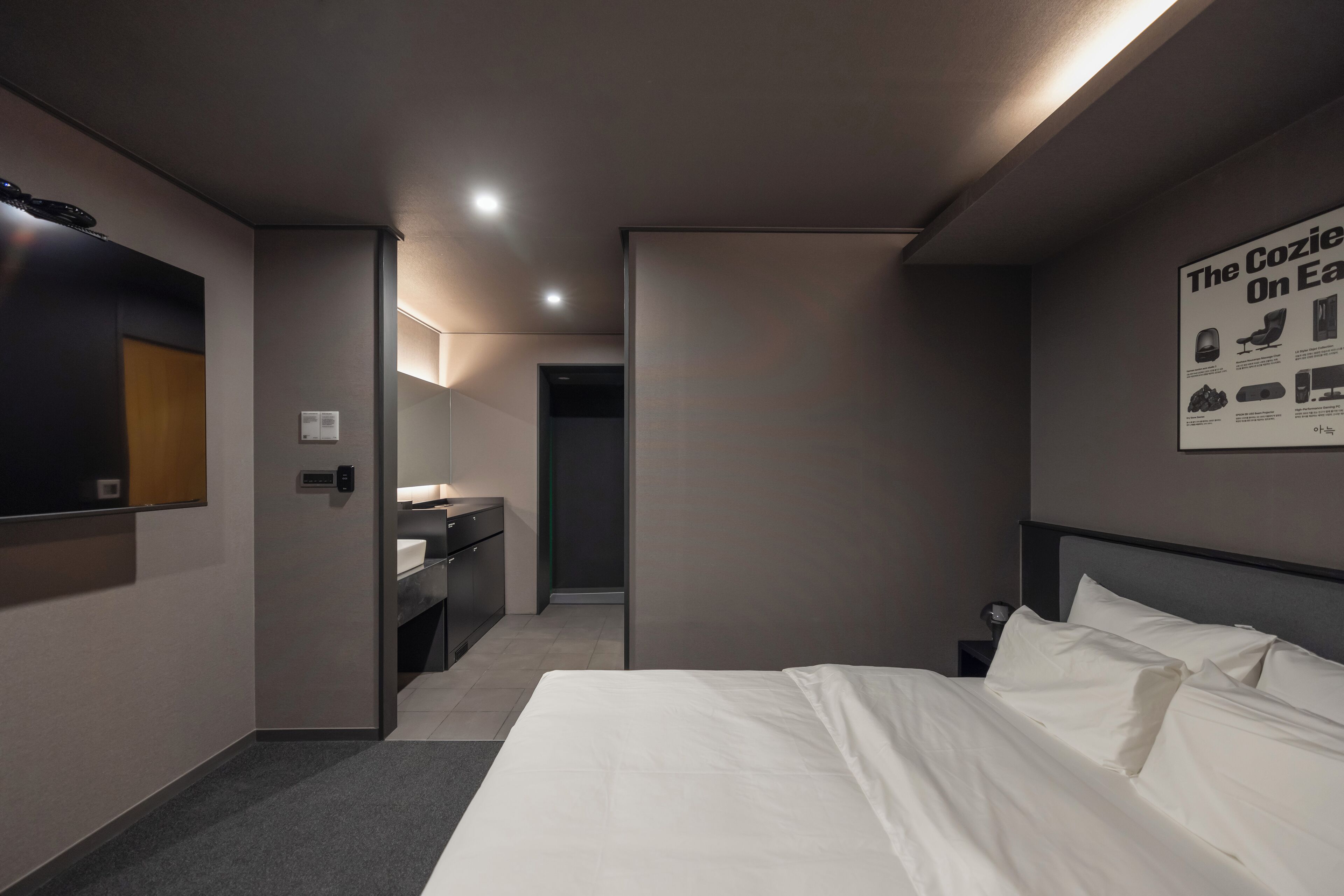 A modern hotel room with a large bed, a desk, and a mirror. There is a poster on the wall and a door leading to another room.
