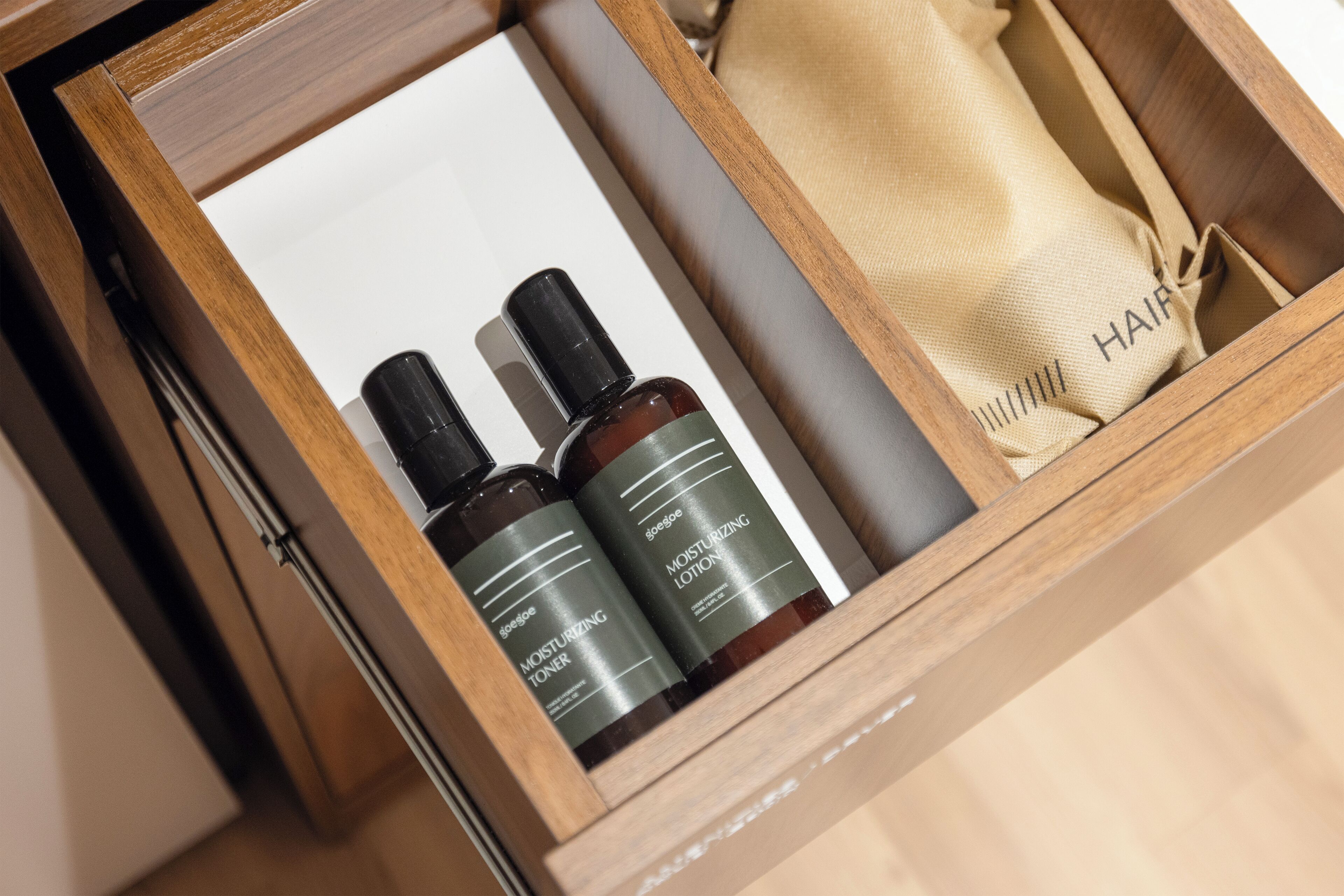 Un tiroir en bois contenant deux flacons de lotion hydratante à la groseille et un sac en tissu beige étiqueté « CHEVEUX ».