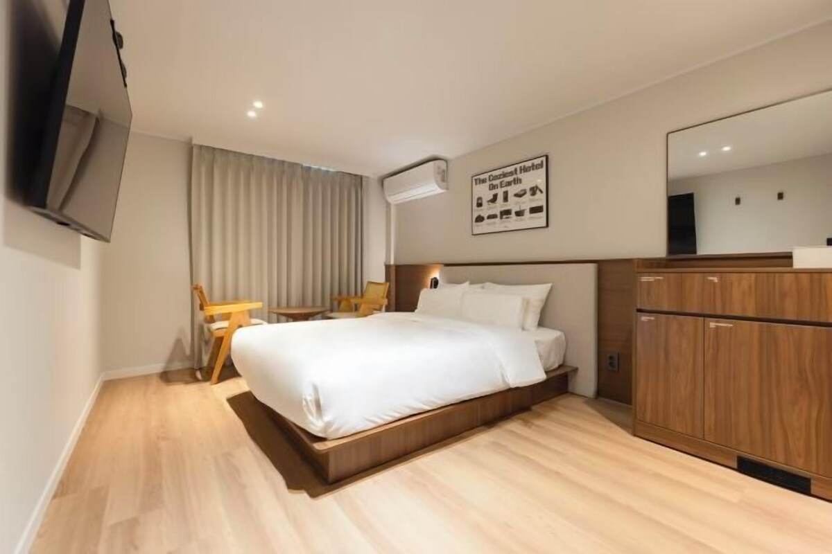 Een hotelkamer met een groot bed, een houten hoofdeinde, een bureau met stoel, een kledingkast en een wandgemonteerde televisie.