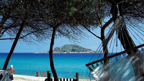Una platja amb un hamaca, una torre de socors i una vista clara del mar i una illa a la distància.
