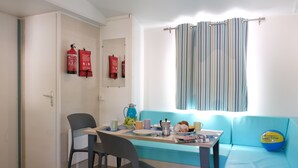 Una habitació amb una taula preparada per l'esmorzar, un sofà blau i una finestra amb cortines a ratlles.