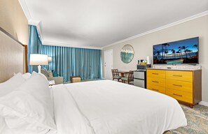 A hotel room with a large bed, a desk with a computer, a television, and a view of palm trees. - Maui Resort Rentals: Marriott's Maui Ocean Club Studio Mountain/Gardenview Suite (Lahaina)