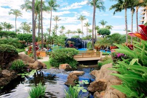 A tropical resort with a waterfall, palm trees, and a small pond with lily pads. - Maui Resort Rentals: Marriott's Maui Ocean Club Studio Mountain/Gardenview Suite (Lahaina)