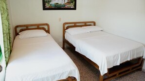 Two single beds with wooden frames and white bedding, a green curtain on the left, and a framed picture of a waterfall on the wall. - hotel casa verde Guatapé (Guatapé)