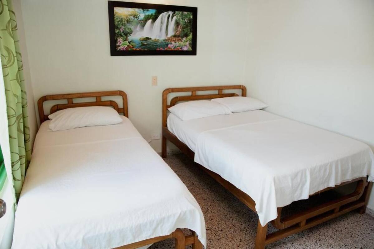 Twee enkele bedden met houten frames en witte beddengoed, een groen gordijn aan de linkerkant, en een lijst met een foto van een waterval aan de muur.