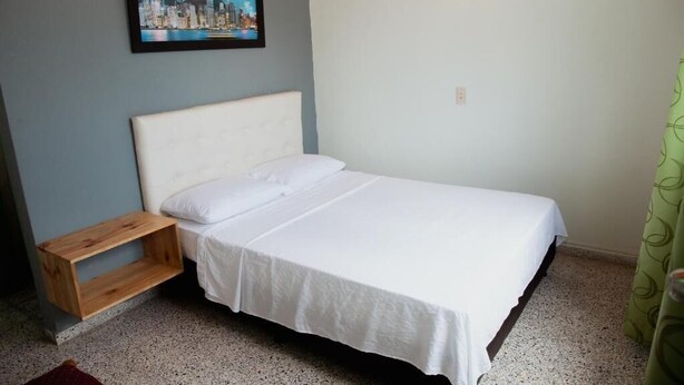 A single bed with a white headboard and bedding, a wooden nightstand, a framed picture on the wall, and a green curtain. - hotel casa verde Guatapé (Guatapé)