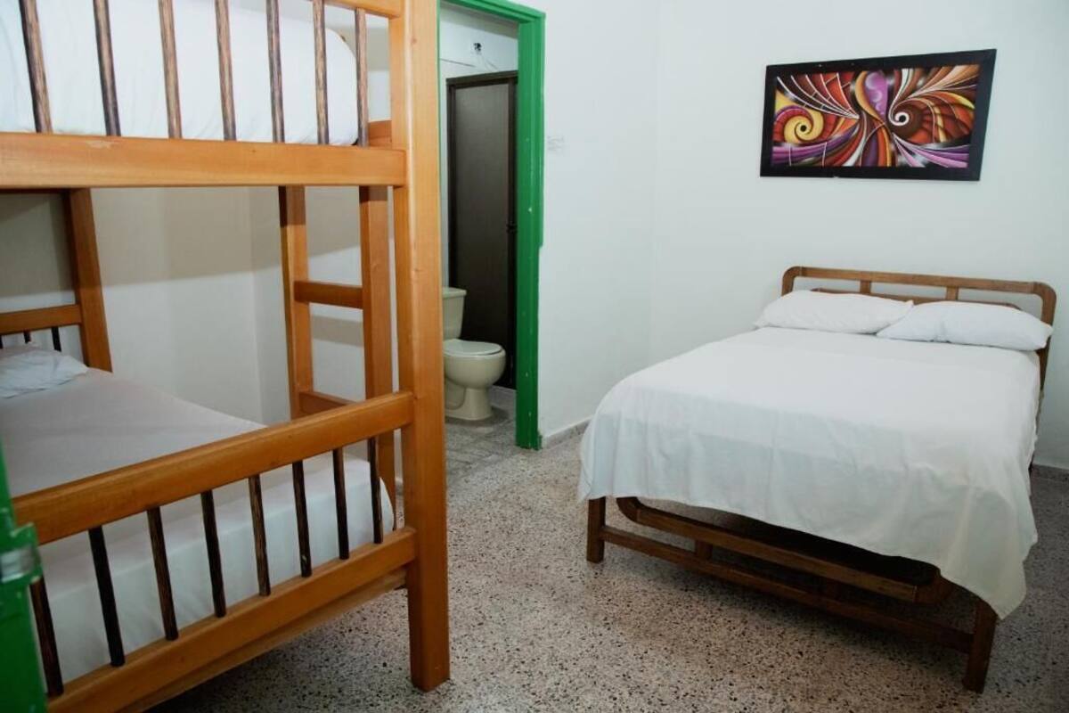 Een kamer met een stapelbed, een enkel bed, een toilet en een kleurrijk abstract schilderij aan de muur.