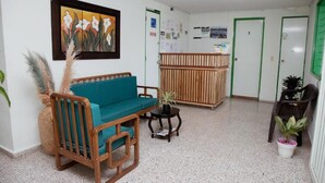 A reception area with a teal sofa, wooden chairs, a small table with a plant, and a reception desk. - hotel casa verde Guatapé (Guatapé)