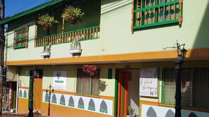 A two-story building with a green and yellow facade, a balcony with plants, and a sign advertising a hotel. - hotel casa verde Guatapé (Guatapé)