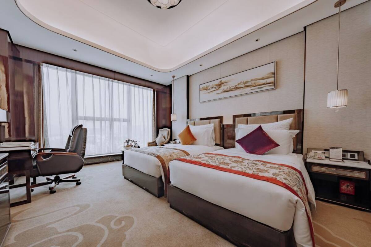 A hotel room with two beds, a desk, a chair, and a large window with curtains.
