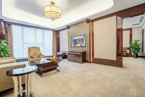 A hotel room with a sofa, a dining table, a desk, and a large window with curtains.