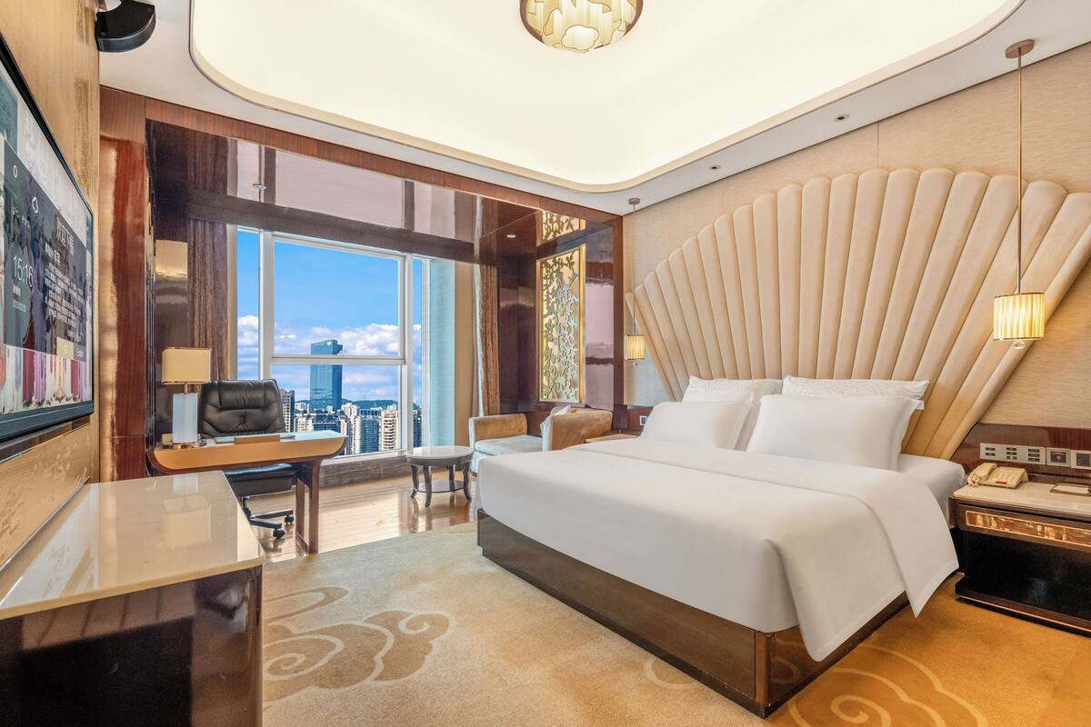 A modern hotel room with a large bed, a desk, and a view of the city.