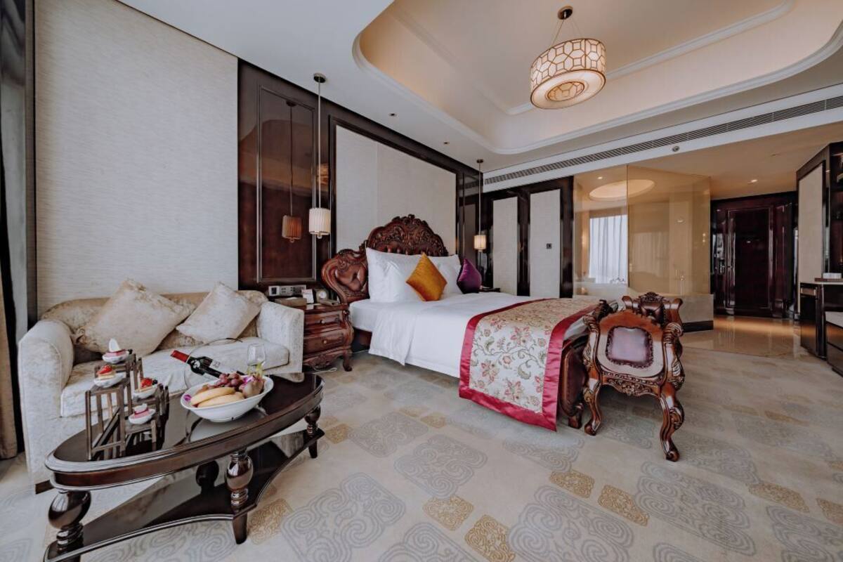 A luxurious hotel room with a large bed, a sofa, a coffee table, and a decorative chair.