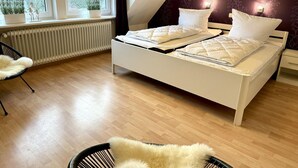 A bedroom with a white bed, a black chair, a radiator, and a window with plants.