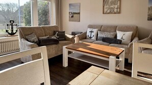A cozy living room with a beige sofa, a wooden coffee table, and a view of greenery outside.