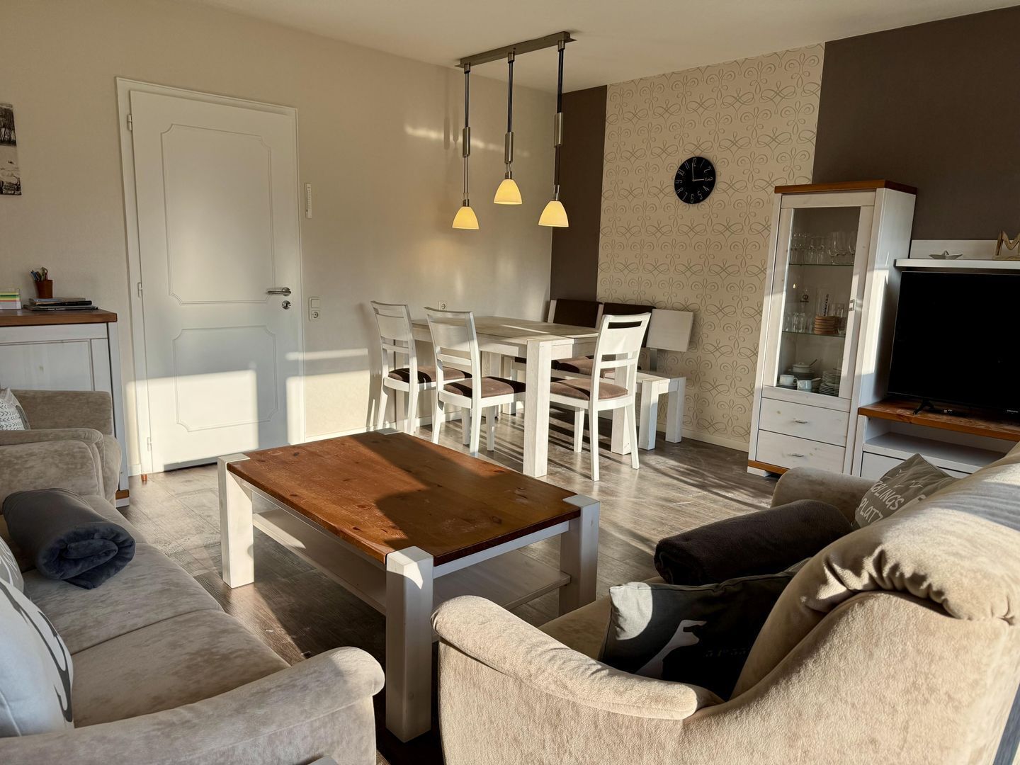 Un salon moderne avec une table basse en bois, des canapés de couleur beige et un coin repas avec des chaises blanches.