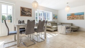 Ein Essbereich mit Tisch und Stühlen, einer Couch und einem kleinen Couchtisch. An den Wänden hängen zwei Gemälde und über dem Tisch hängt eine Chandelier.