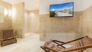 Ein Spa-Raum mit einem großen Fernseher an der Wand, einer Holzbank und einer Duschkabine aus Glas.