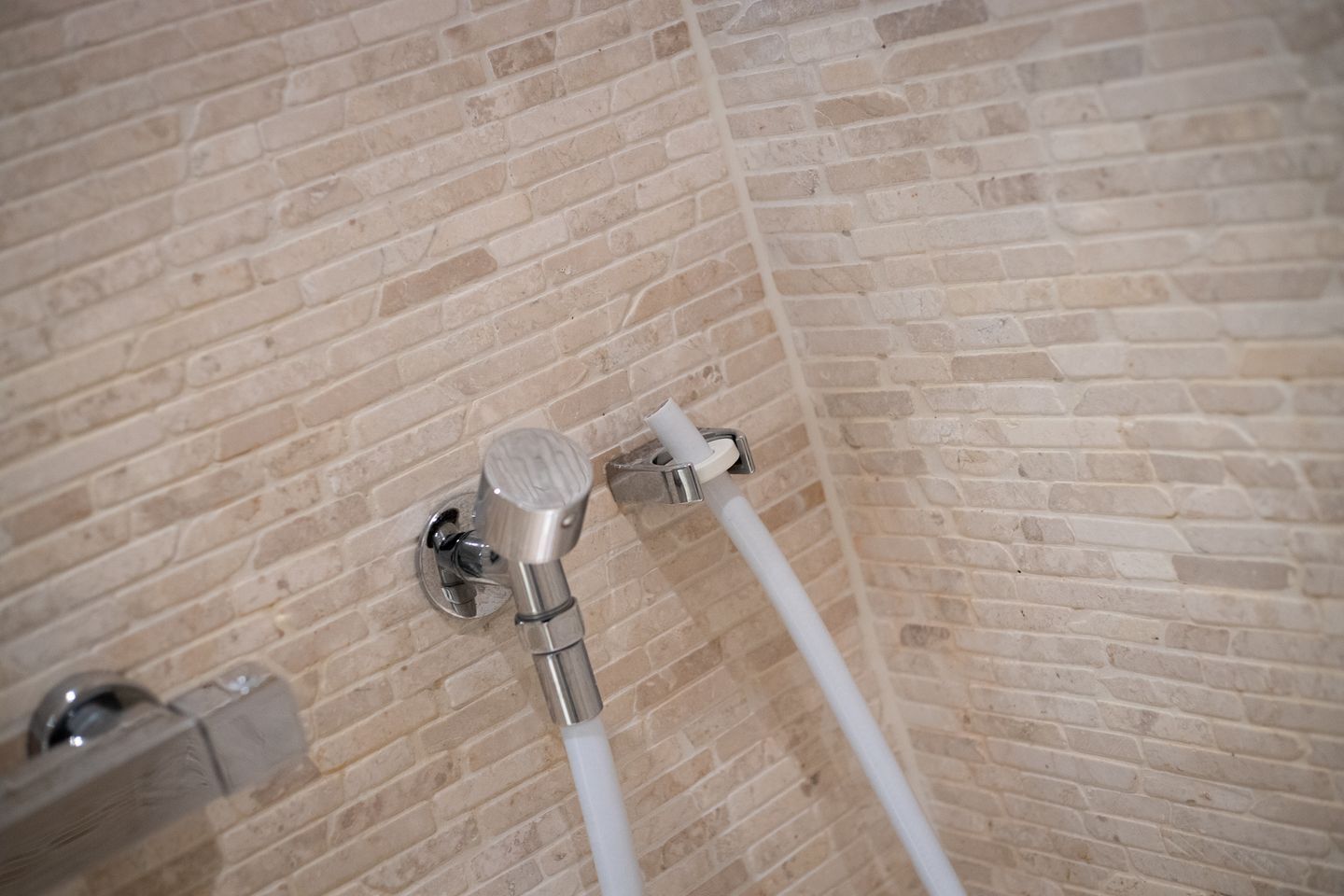 A shower with a metal handle and a white pipe against a brick wall.