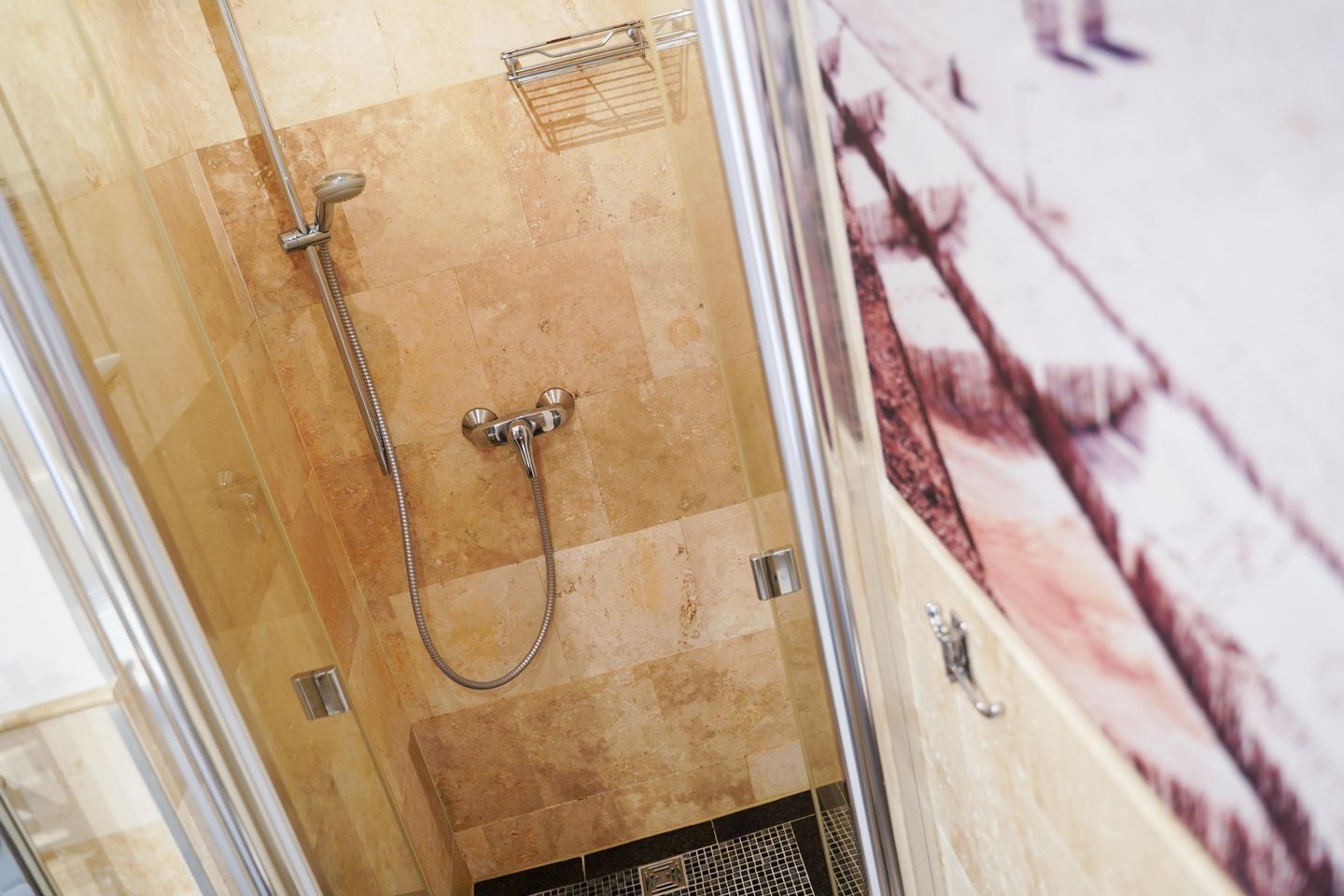 A shower with a handheld showerhead and a wall-mounted faucet, a tiled shower floor, and a glass door.