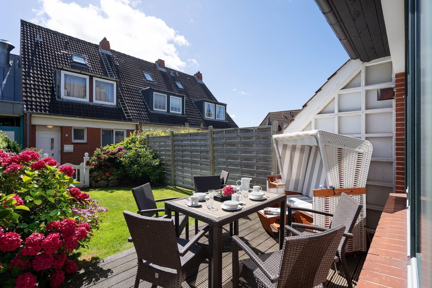 A patio with a table set for dining, surrounded by wicker chairs and a white umbrella.