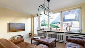 A living room with a brown leather sofa, a wooden coffee table, and a TV mounted on the wall. - Meeresstern - Beautiful house for 6 pers. with terrace, parking space, WLAN. (Westerland)