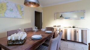 A dining area with a wooden table set for four, a large map on the wall, and a kitchen area with a wooden cabinet and a mirror above it. - Meeresstern - Beautiful house for 6 pers. with terrace, parking space, WLAN. (Westerland)