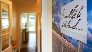 A hallway with a sign that reads "Endlich Urlaub..." and a view of a beach with white buildings. - Meeresstern - Beautiful house for 6 pers. with terrace, parking space, WLAN. (Westerland)
