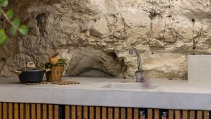 A rustic kitchen with a stone wall, a sink, a pot, and a basket with a pomegranate. - Villa with heated pool located in a unique position (Modica)