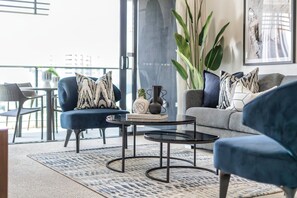 A modern living room with a sofa, armchairs, a coffee table, and a large plant.