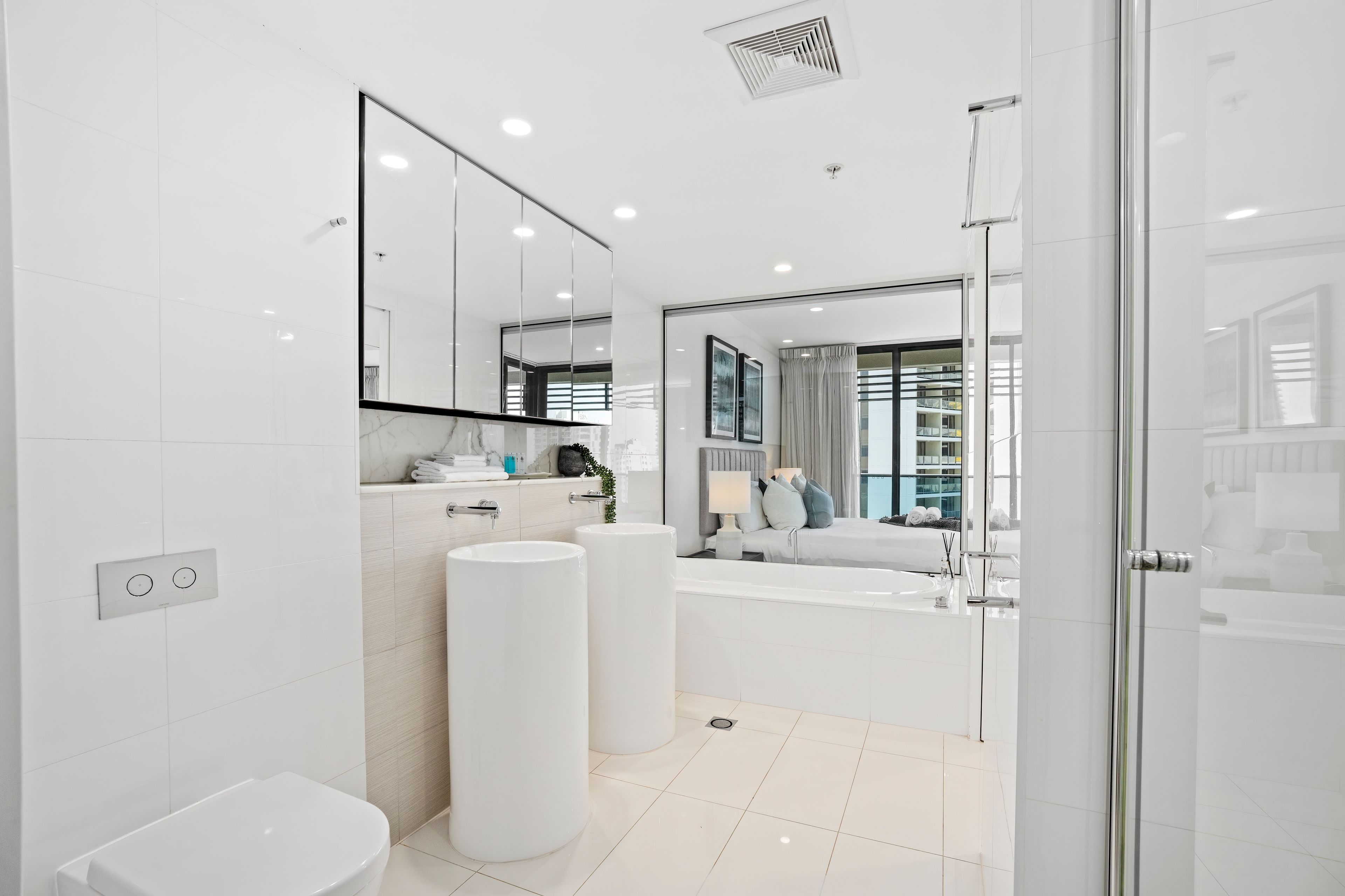 Een moderne badkamer met een toilet, twee wasbakken, een spiegel en een douche.