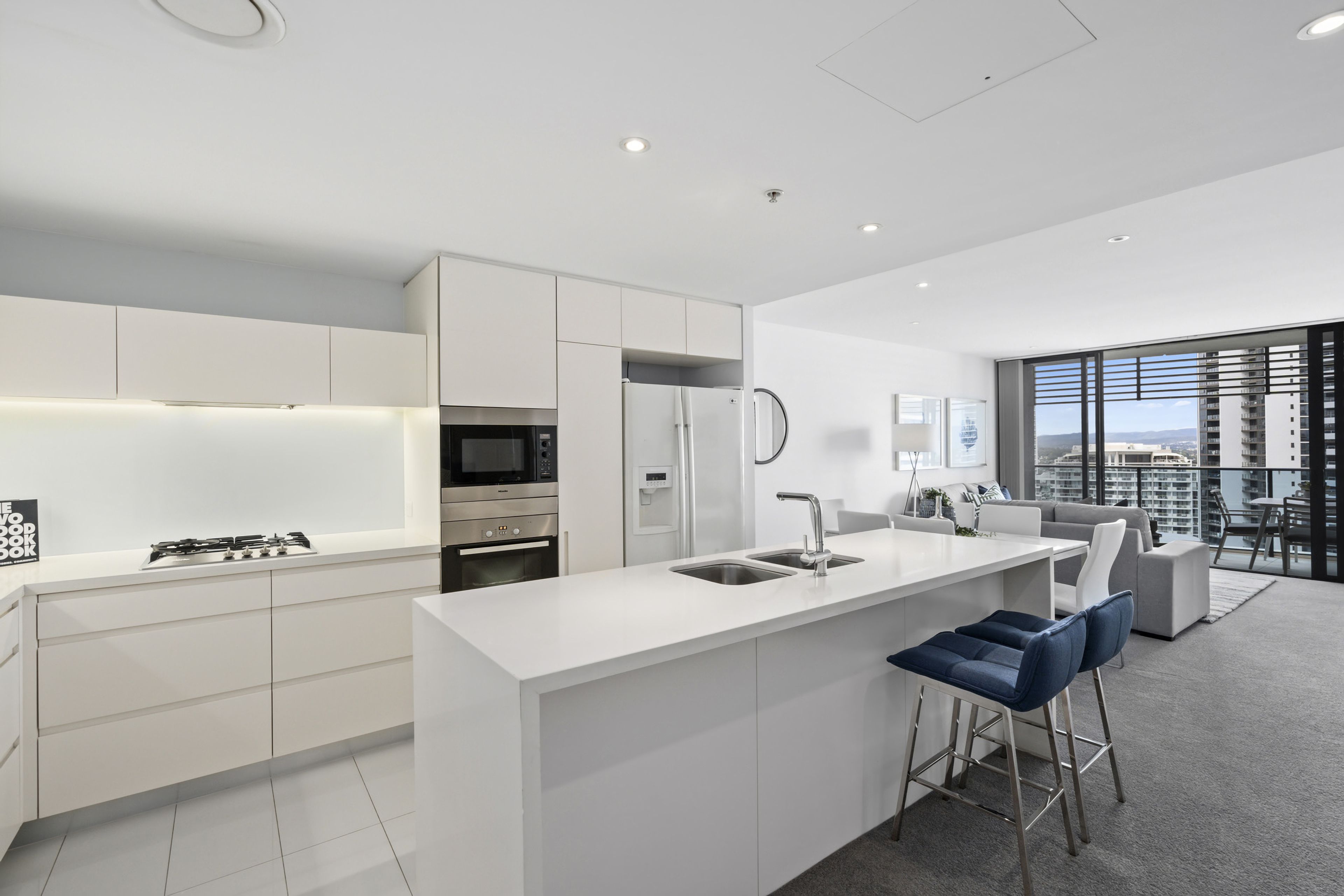A modern kitchen with a central island, stainless steel appliances, and a view of the city through large windows.