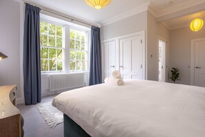 A bedroom with a large bed, a window with curtains, a radiator, and a door.