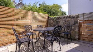 Un patio con una mesa redonda y seis sillas, rodeado por una valla de madera y un muro de piedra.