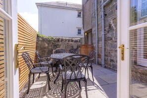 Un patio al aire libre con una mesa redonda y seis sillas, una valla de madera y un muro de piedra.