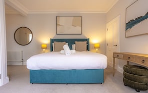 A neatly arranged bedroom with a large bed, two bedside lamps, a round mirror, a framed abstract painting, and a wooden nightstand. - Skye Sands | Westview House | St Andrews (St Andrews)