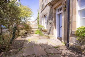 A stone pathway leading to a traditional building with a white door and a hanging light fixture.