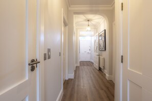 A hallway with white walls, a wooden floor, and a door at the end leading to a room. - Skye Sands | Westview House | St Andrews (St Andrews)