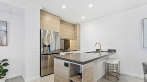 Cozinha moderna com geladeira de aço inoxidável, forno embutido e ilha de madeira com banquetas.