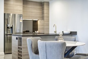 A modern kitchen with a central island, stainless steel appliances, and a dining area with grey upholstered chairs.