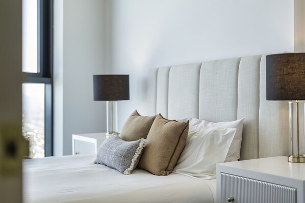 A neatly made bed with two pillows and a bedside table with a lamp.