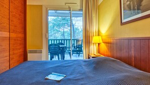 A hotel room with a bed, a window with curtains, a table with a lamp, and a painting on the wall. - Les Grands Pins by Interhome (Maubuisson)