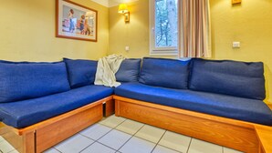 A room with a blue sofa, a framed picture on the wall, and a window with curtains. - Les Grands Pins by Interhome (Maubuisson)