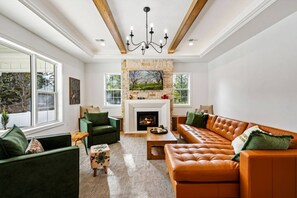 Ein Wohnzimmer mit Kamin, grünen und braunen Ledersofas, einem Holztisch und einer Chandelier.