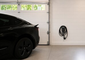 A car parked in a garage with a white door and a charging cable on the wall. - Luxury Meets Location | Near Ephraim & Sister Bay (Ephraim)