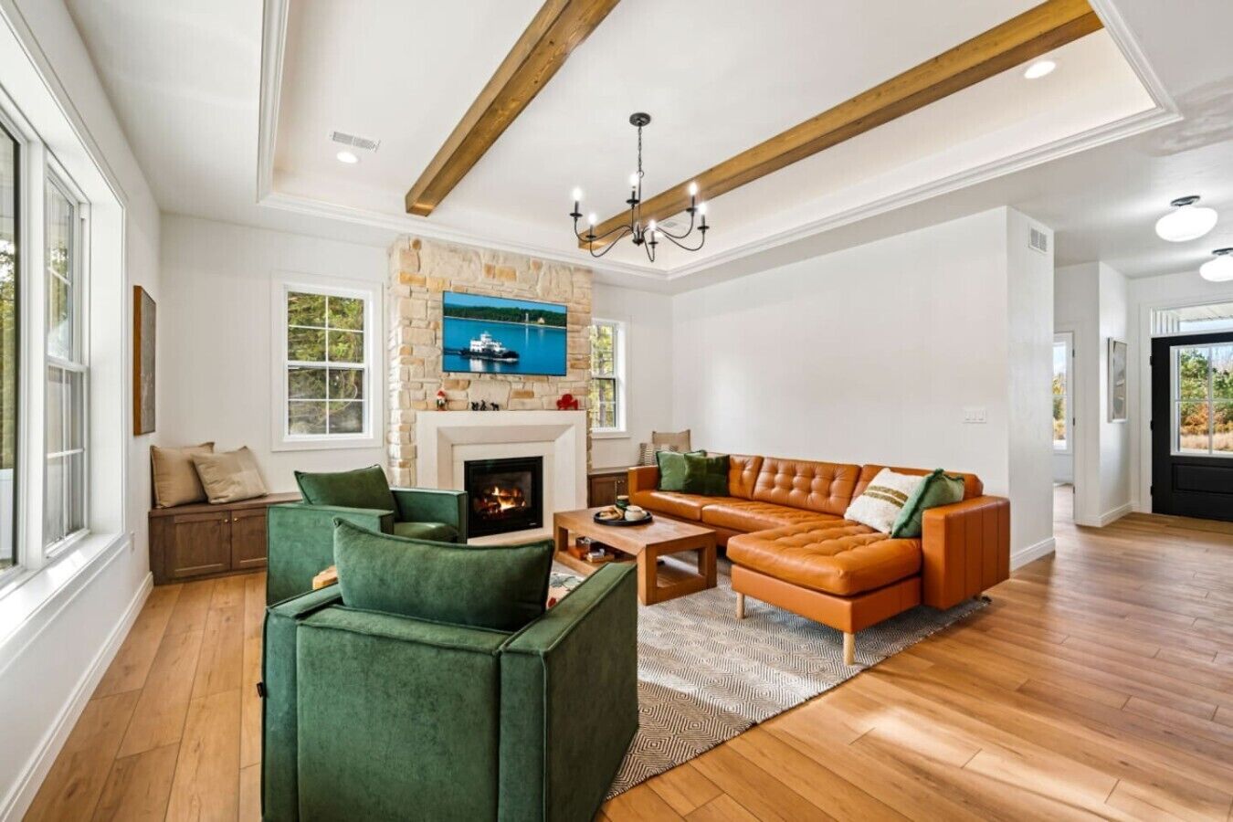 A spacious living room with a fireplace, green armchairs, a leather sofa, and a large window.