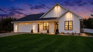 A modern two-story house with a garage, large windows, and a well-lit front porch. - Luxury Meets Location | Near Ephraim & Sister Bay (Ephraim)