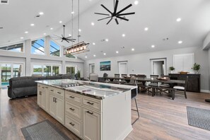 A spacious kitchen with a large island, modern pendant lights, and a dining area with a wooden table and chairs. - Spacious Lake Tarpon Getaway (Palm Harbor)