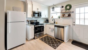 Una cocina moderna con armarios blancos, electrodomésticos de acero inoxidable, un horno negro y una encimera de granito. Hay una alfombra blanco y negro en el suelo.